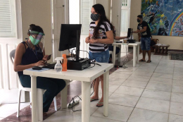 Imagem: Estudante mulher em pé no salão da Reitoria, recebendo o chip de uma servidora mulher que está sentada em uma cadeira de frente para um computador (Foto: Norton Falcão/UFC)