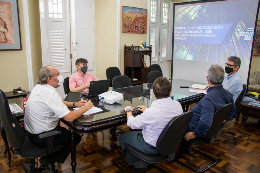 Reitor e membros do SEBRAE sentados em volta de uma mesa; ao fundo há uma tela com apresentação de slides (Foto: Ribamar Neto/UFC)