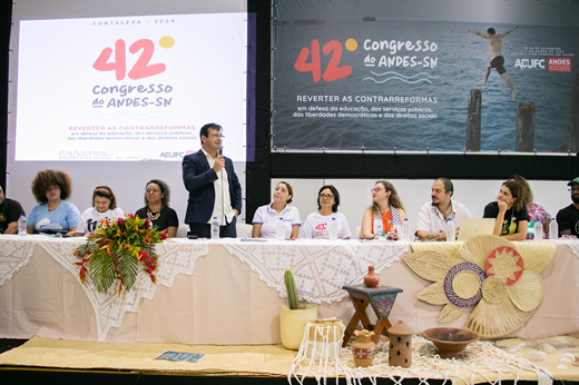 Imagem: De pé, o reitor Custódio Almeida discursa aos presentes na abertura do 42º Congresso do ANDES-SN; ao seu lado, estão os demais membros da mesa solene. (Foto: Álvaro Graça Jr./ UFC Informa)