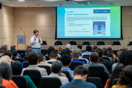 Imagem: De pé, na frente do auditório, o Prof. Enrique Rodriguez-Castellón ministra palestra. O público encontra-se de costas para a câmera, em primeiro plano. (Foto: George Lucas/ FIEC)