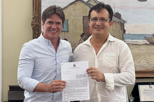 Imagem: Prefeito Herberlh Mota e reitor Custódio Almeida posam segurando o termo de cooperação entre a Prefeitura de Baturité e a UFC.