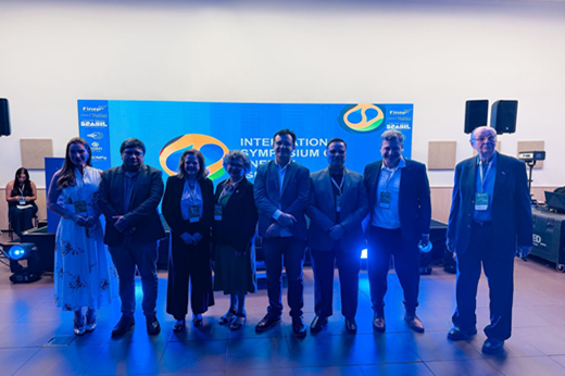 Imagem: Oito pessoas de pé em frente ao palco, dentre elas o reitor Custódio Almeida, a vice-reitora Diana Azevedo, o coordenador do evento Enio Pontes e o professor do MIT Nolan Browne.