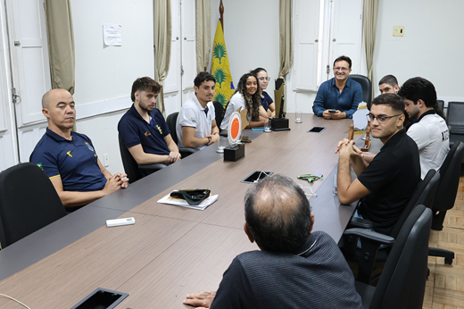 Imagem: Reitor, gestores da Secretaria de Esportes e estudantes-atletas sentados à mesa durante a reunião