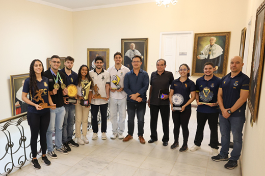 Imagem: De pé, na entrada do Gabinete da Reitoria, oito atletas (três jovens do sexo feminino e cinco do sexo masculino) posam junto com o reitor Custódio Almeida, o secretário Antônio Lima e o secretário-adjunto Wildner Lins