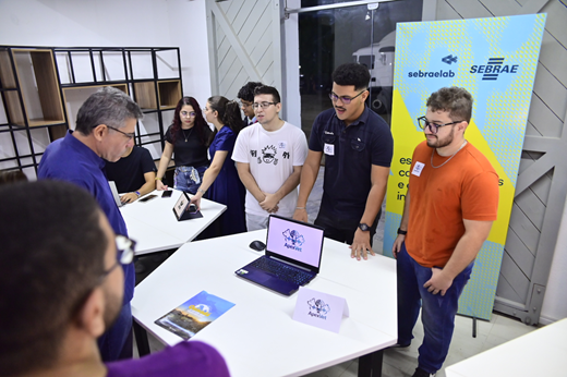 Imagem: De pé, no interior da Estação Tecnológica, representantes da start-up Apexvet apresentam sua proposta aos visitantes. Sobre a mesa, está um notebook; atrás deles, um banner do Sebrae.