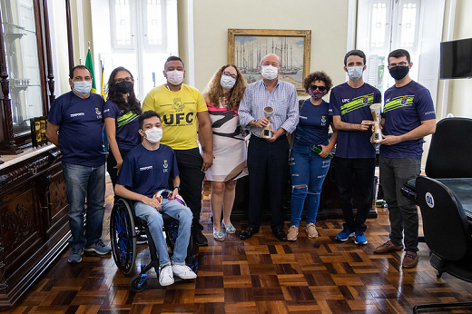 Pessoas posando para a foto lado a lado no Gabinete da Reitoria, com obra de arte ao fundo