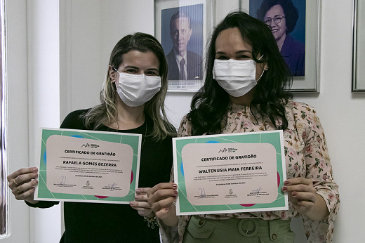 Servidoras em pé, lado a lado, seguram certificados de gratidão para foto