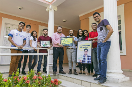 Imagem: foto de pessoas em pé reunidas para foto segurando as novas identidades visuais da agência de estágios