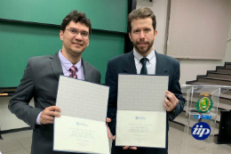 Imagem: Foto de dois homens brancos, de paletó e gravata, segurando placas de homenagem