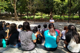 Imagem: Foto de pessoas sentadas no chão, de costas, assistindo a uma palestra