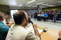 Imagem: Pesquisadores falando e pessoas sentadas formando a plateria durante evento no auditório da Reitoria