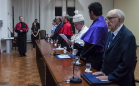 Reitor Henry Campos realiza discurso durante cerimônia, com participantes da mesa de pé