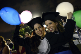 Imagem: Duas concludentes sorrindo e vestidas de beca no dia da colação segurando balões nas mãos