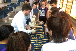 Imagem: Foto de visitantes em evento anterior observando osso sobre uma mesa