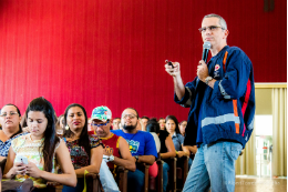 Imagem: Foto de palestrante do SAMU apontando passador de slides a partir da plateia do simpósio. Ao lado dele, pessoas sentadas nas cadeiras do auditório