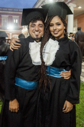 Imagem: Casal de jovens vestidos de beca no jardim da Reitoria