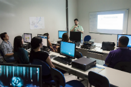 Imagem: professor dá aula a frente de alunos em laboratório de informática