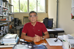 Imagem: foto de um homem de camisa vermelha sentando em um escritório com livros e pesquisas