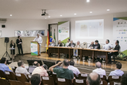 Foto do auditório cheio de gente e, à frente, os integrantes da mesa na abertura do evento