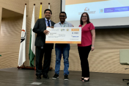 Imagem: foto do estudante vencedor com equipe julgadora segurando um cheque 