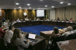 Imagem: Foto de pessoas sentadas em cadeiras em formato de círculo. Ao centro, um tapete azul