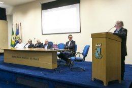 Imagem: Foto de homens sentados em uma mesa em um palco e, em destaque, outro homem em um púlpito