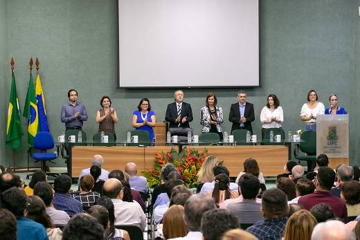 Imagem: foto do palco de uma auditório com pessoas em pé atrás de uma mesa de solenidade