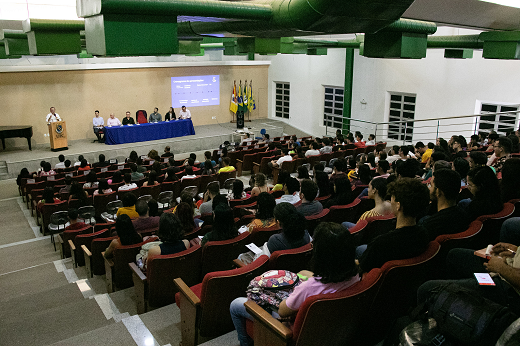 Imagem: Alunos sentados em um auditório; à frente, na parte elevada, está a mesa do evento composta por professores da UFC; o reitor está de pé, falando ao microfone (Foto: Ribamar Neto/UFC)