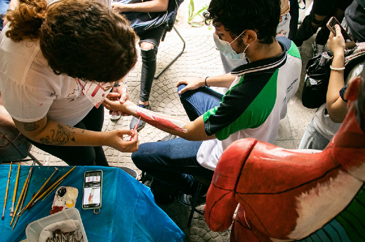 Imagem: Foto de uma acadêmica de Medicina pintando com tinta as fibras musculares no braço de um jovem durante o Anatomy Day