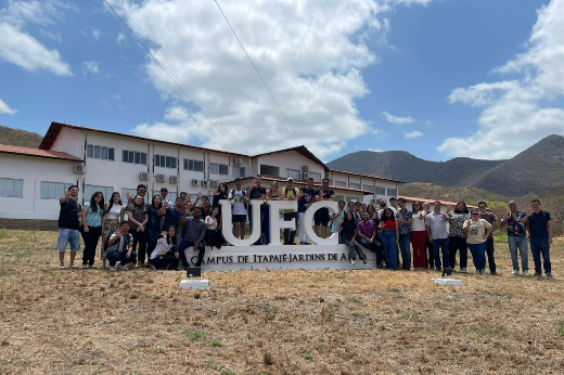 Imagem: foto de várias pessoas jovens em pé ao lado da sigla UFC. Ao fundo, prédio do campus da UFC em Itapajé