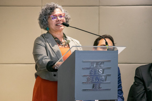 Imagem: Foto bem aproximada da vice-reitora Diana Azevedo discursando no púlpito