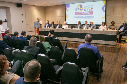 Imagem: Foto da vice-reitora Diana Azevedo discursando no púlpito, com a mesa de autoridades ao fundo e o painel com a identidade visual do evento