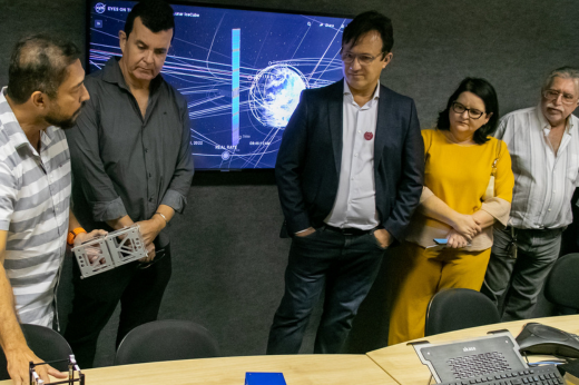 Imagem: Um grupo de pesquisadores, entre eles o retiro, sendo apresentados a um dos equipamentos do laboratório