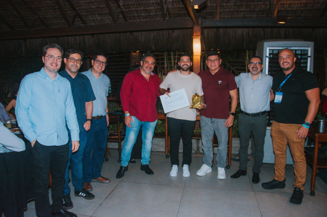 Oito homens posam para foto. Ao centro, de blusa branca, um jovem segura um certificado