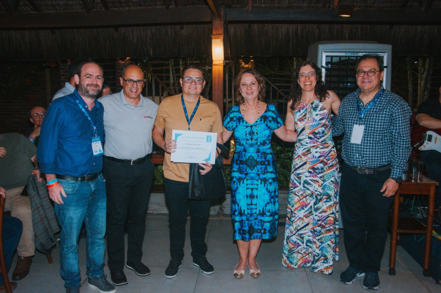 Seis pessoas posam para foto. Ao centro, um jovem segura um certificado