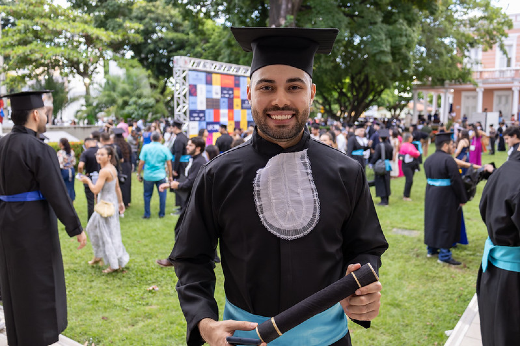 Imagem: Jovem usando beca posa para foto no jardim da Reitoria 