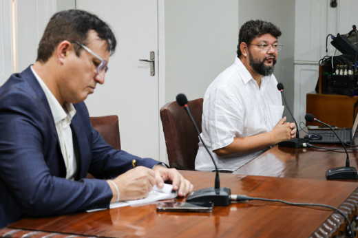 Prof. Rafael dos Santos sentado, falando ao microfone, e o reitor Custódio Almeida, ao lado, fazendo anotações