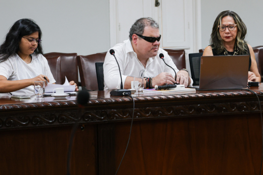 Três membros da Comissão sentados, falando durante a reunião