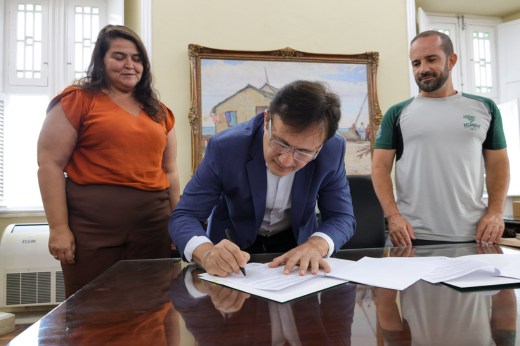 Imagem: Foto do reitor Custódio Almeida curvado assinando um documento