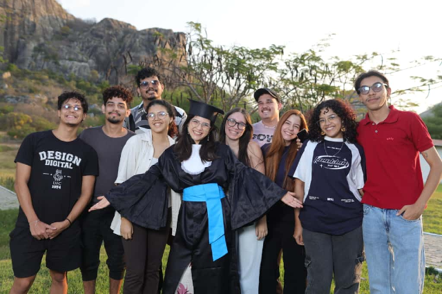 Imagem: jovem de beca rodeada por amigos 