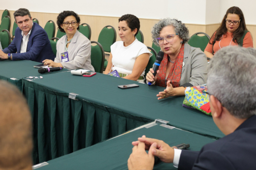 Imagem: Foto da vice-reitora Diana Azevedo discursando com microfone na mesa do evento