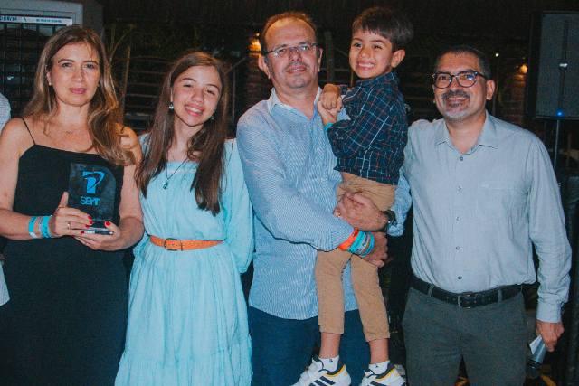 Imagem: cinco pessoas posam para foto. Um homem (ao centro) segura um menino no colo