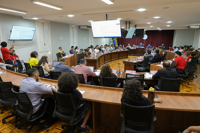 Imagem: membros da administração superior e demais integrantes sentado ao redor das mesas do consuni