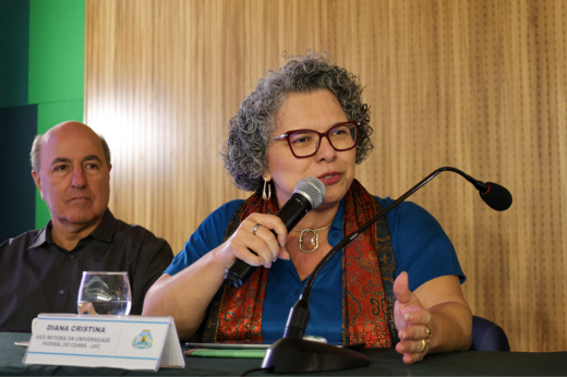 Imagem: Foto na qual a vice-reitora Diana Azevedo discursa com o microfone