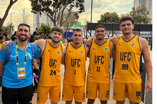 Quatro jogadores homens de basquete uniformizados e um treinador abraçados lateralmente