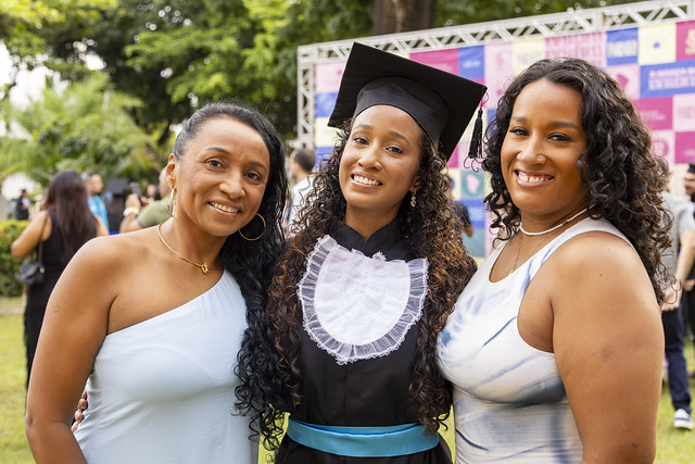 Imagem: jovem negra vestida com beca posa para foto abraçada entre outras duas jovens negras