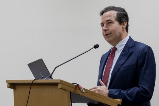 Imagem: Foto de plano fechado com o professor José Macêdo, da UFC, discursando no púlpito, vestido de terno e gravata