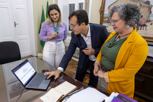 Imagem: Foto em que o reitor Custódio Almeida utiliza um computador para publicar o resultado final, estando acompanhado da vice-reitora Diana Azevedo e da presidente da CCV, Luana Sombra