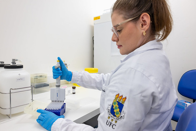 Imagem: Foto de pesquisadora utilizando jaleco e luvas de proteção dentro do laboratório