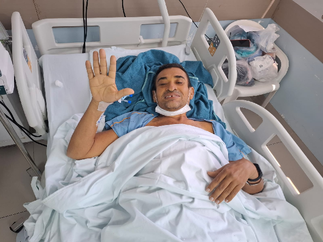 Imagem: Homem deitado em cama de hospital acena e sorri (Foto: Marília Rêgo)